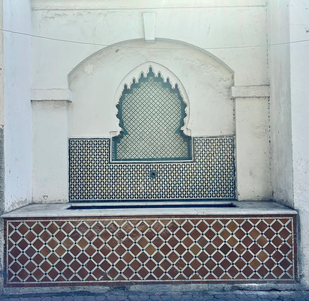 Fonte de parede no bairro Habous, em Casablanca, com arco recortado branco sobre painel de azulejos.