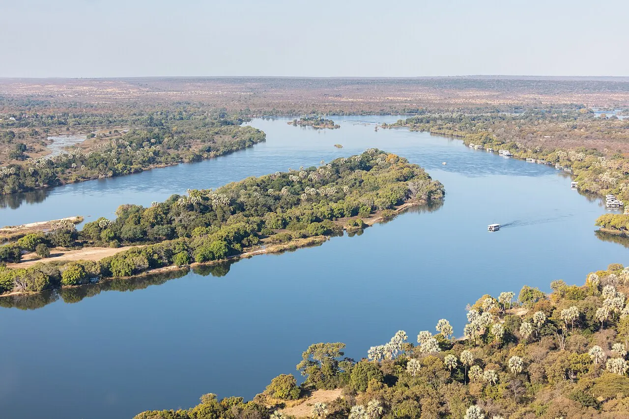 Le large fleuve bleu se divise en bras autour de longues îles boisées, avec un petit bateau sur l'eau et la plaine qui s'étend jusqu'à l'horizon.