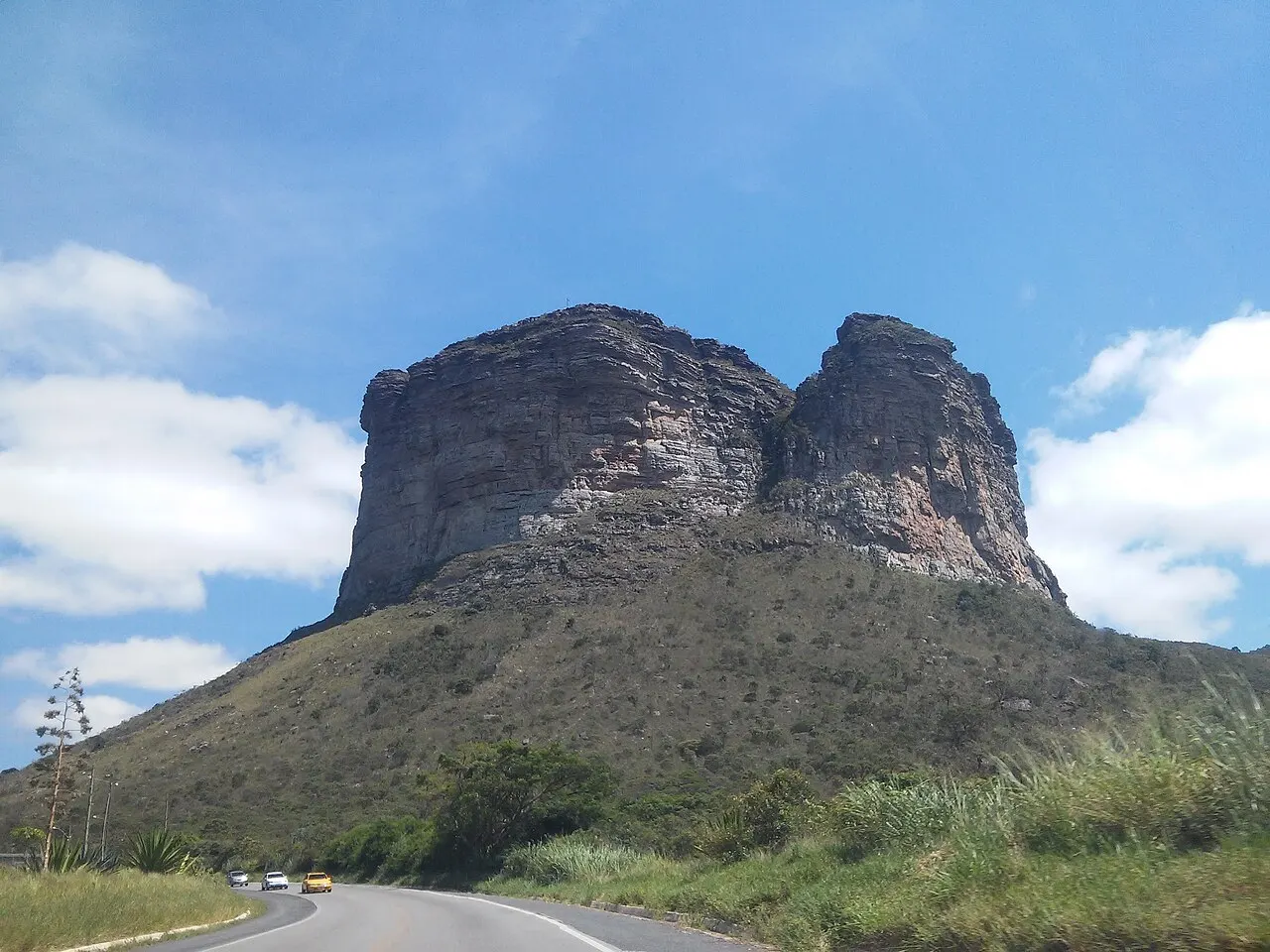 O Morro do Pai Inácio, de topo plano e paredões de arenito, visto da estrada que passa ao pé dele, sob céu azul.