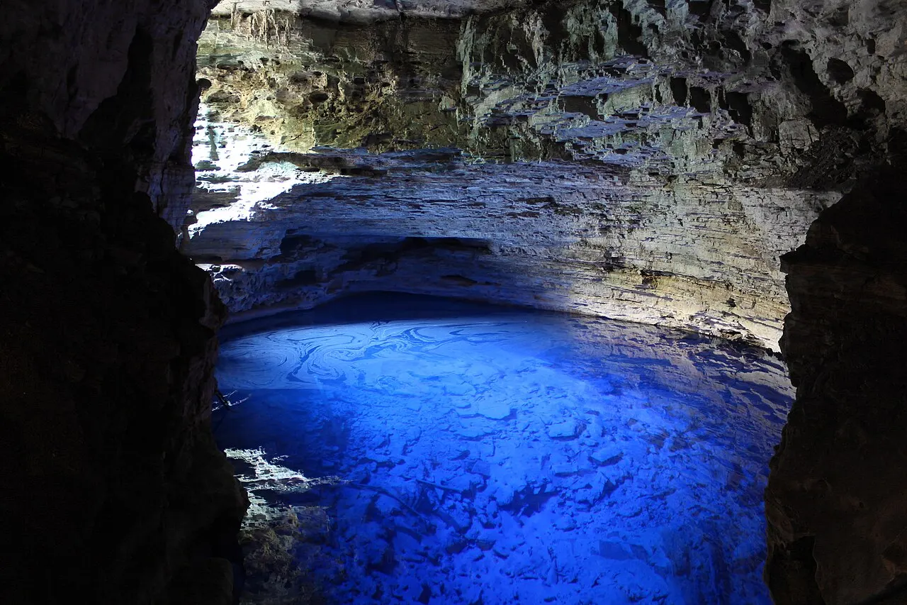 A água de um azul intenso do Poço Encantado, iluminada no fundo da gruta escura.