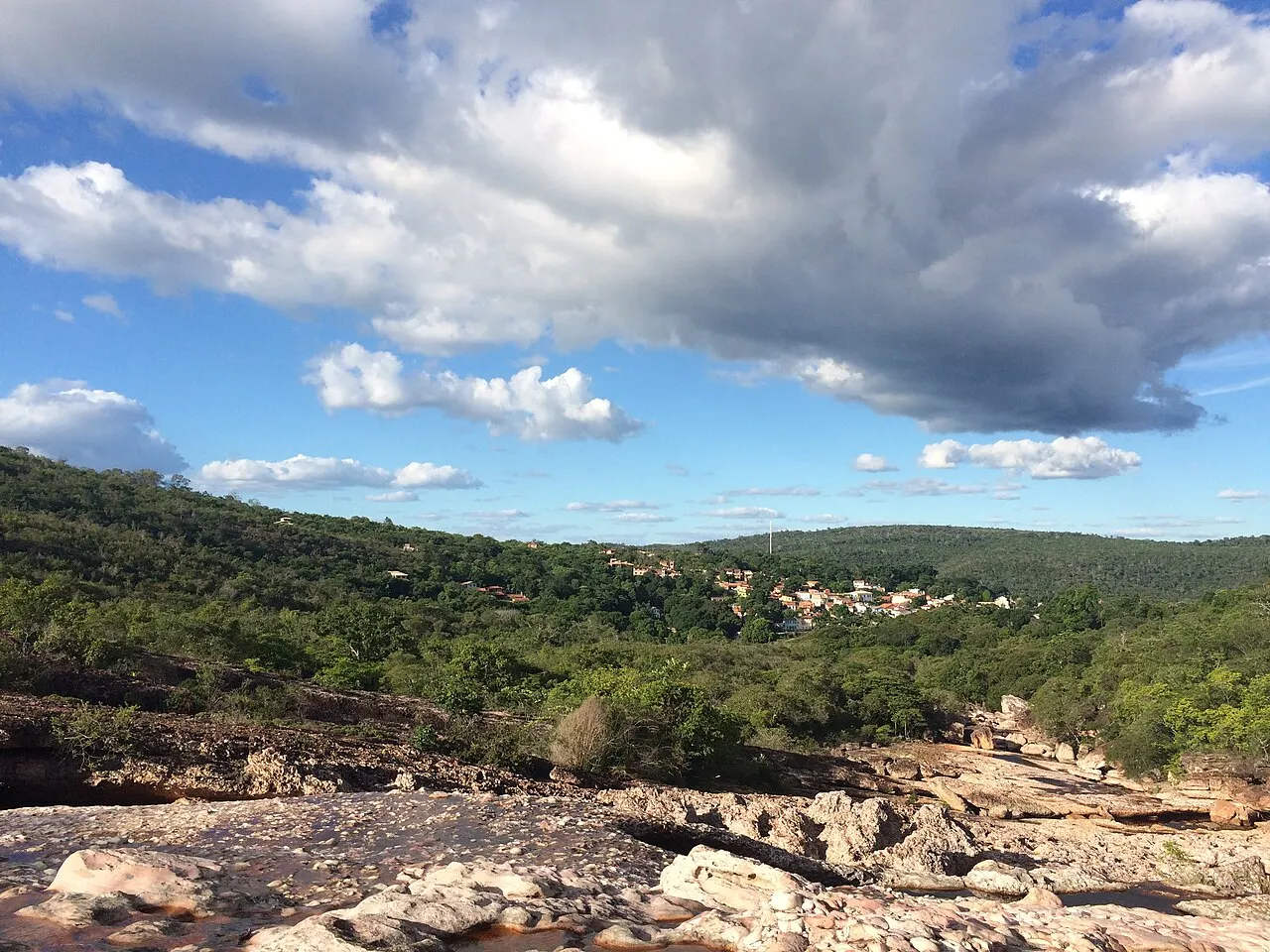 As lajes de pedra do Serrano em primeiro plano, com os morros verdes e as casas de Lençóis ao fundo, sob nuvens.