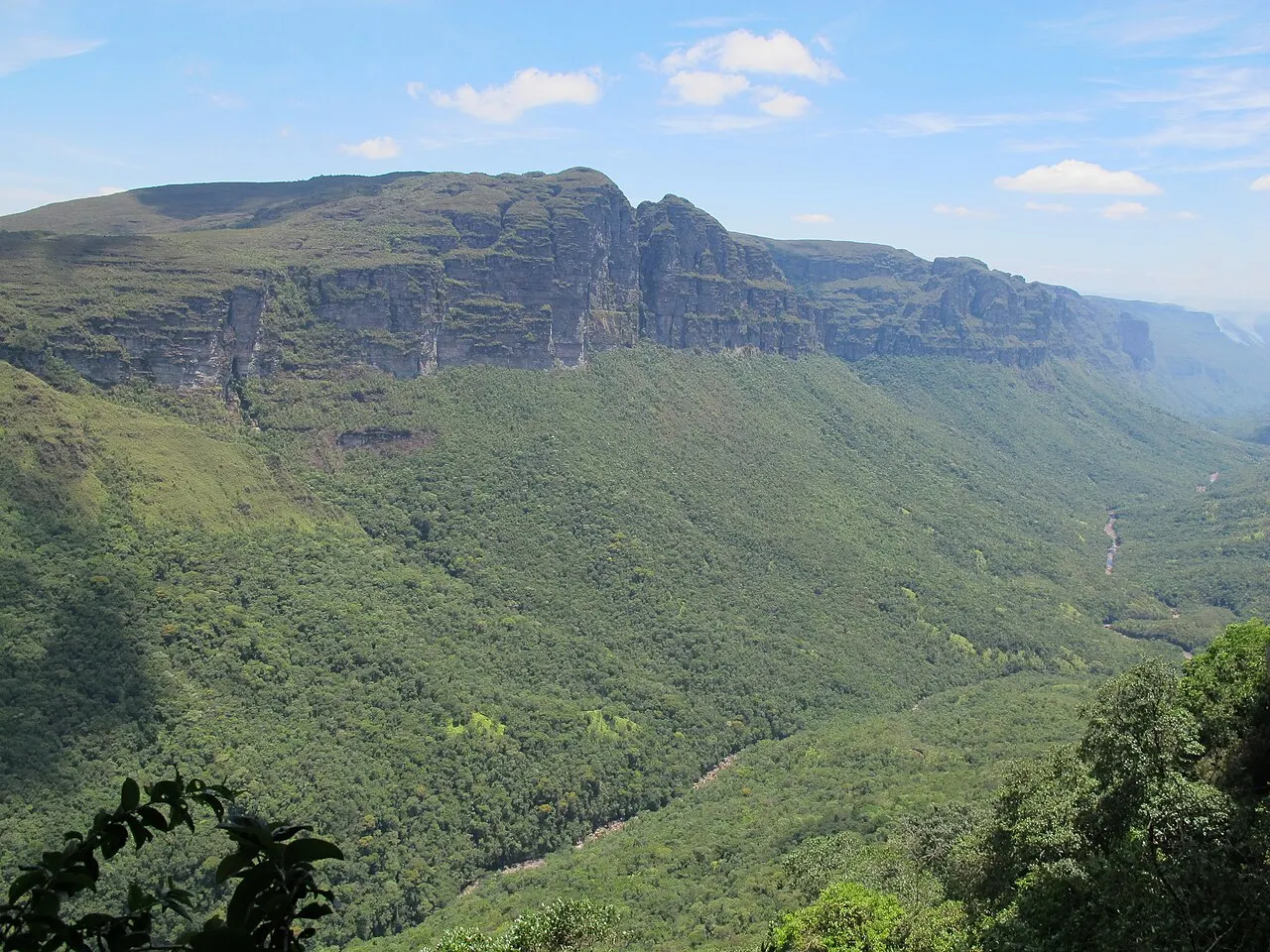 O Vale do Pati coberto de mata verde, cercado de paredões de pedra, visto de cima num dia de céu azul.