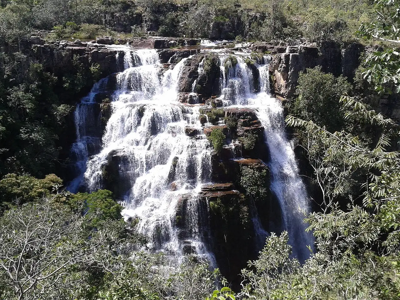 A água da Cachoeira Almécegas descendo em vários degraus de pedra entre a vegetação do cerrado.