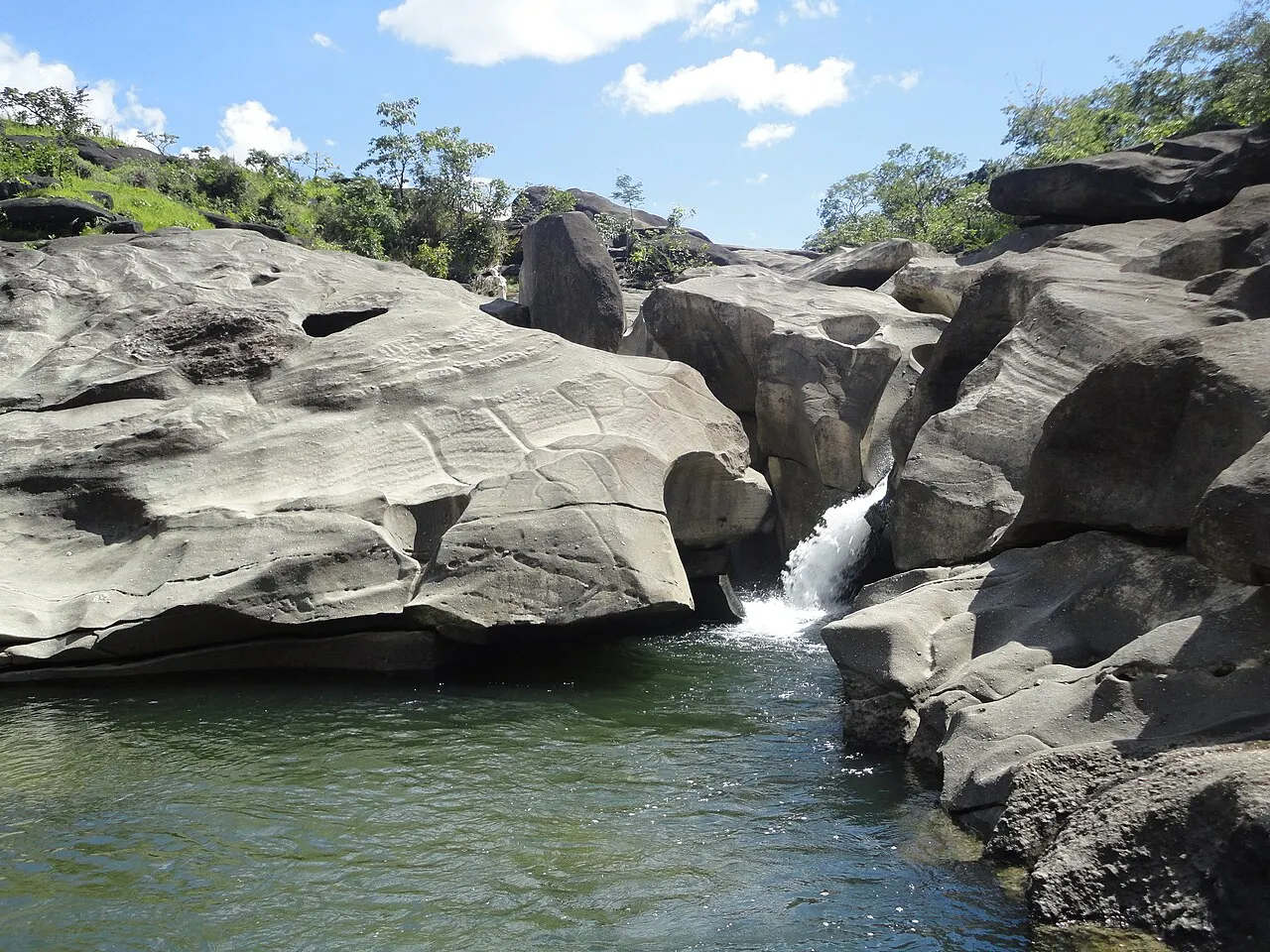 A água verde do rio correndo entre as rochas cinzentas e lisas do Vale da Lua, com uma pequena queda ao fundo.