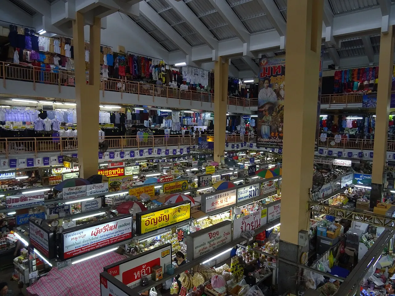 O interior do Mercado Warorot tem bancas no térreo, roupas penduradas no andar de cima e colunas altas.
