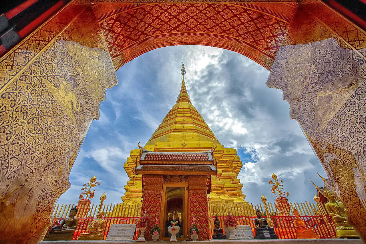 Chedi coberto de ouro com guarda-sóis dourados, visto através de um arco decorado.