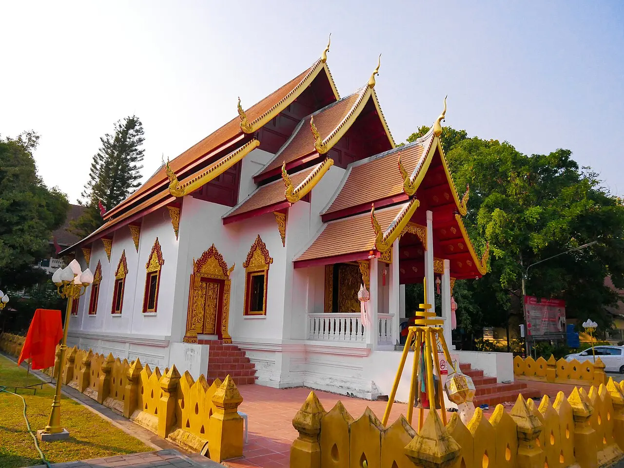Templo de paredes brancas e telhados vermelhos em camadas, com flores amarelas à frente.