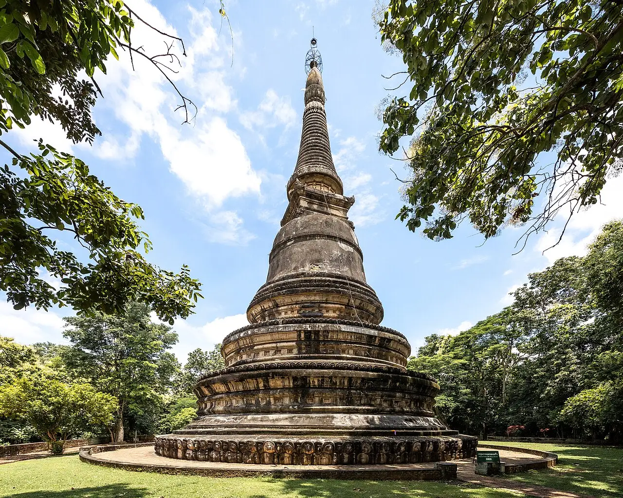 Chedi alto e pontiagudo de tijolo escuro e musgo, entre árvores, sob céu azul.