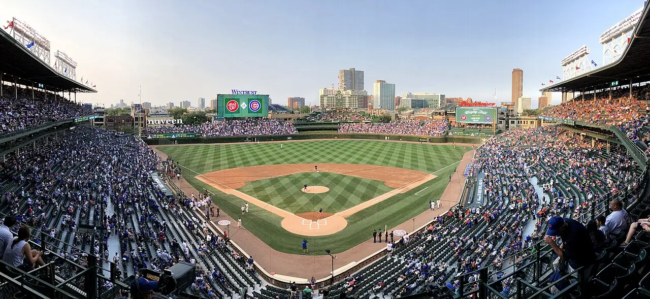Wrigley Field visto das arquibancadas, com o campo, as duas laterais cheias e a cidade atrás do placar.