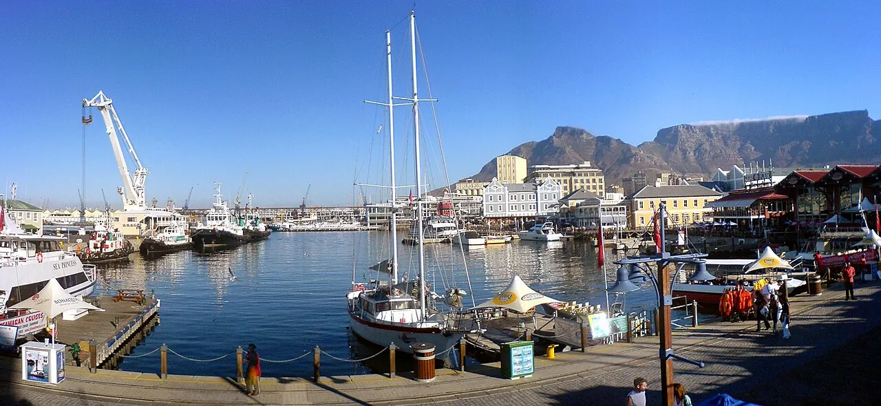 A doca do V&A Waterfront reúne veleiros, um guindaste e a Montanha da Mesa ao fundo.