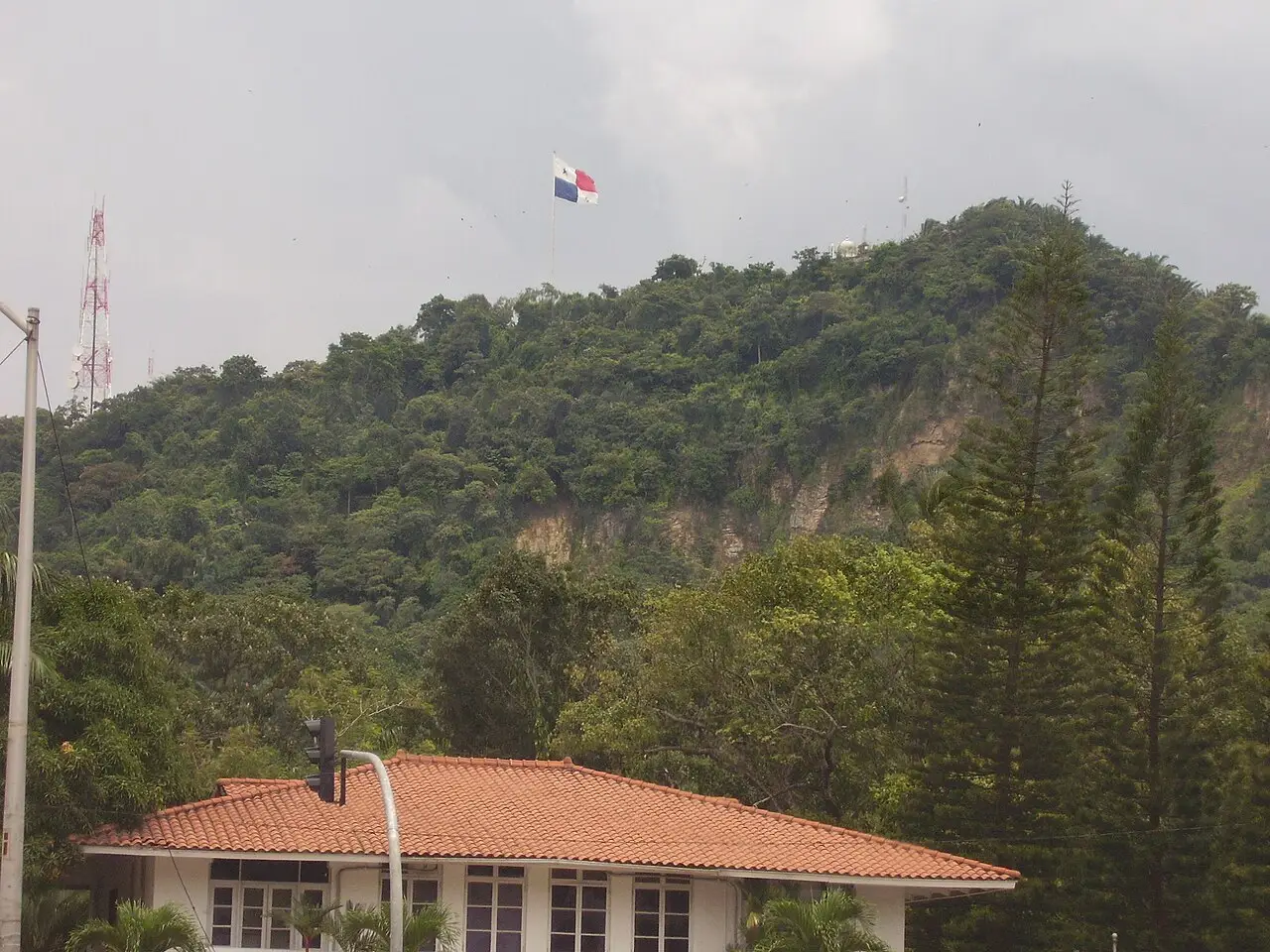A bandeira do Panamá hasteada acima de um morro verde, com telhados vermelhos no primeiro plano.
