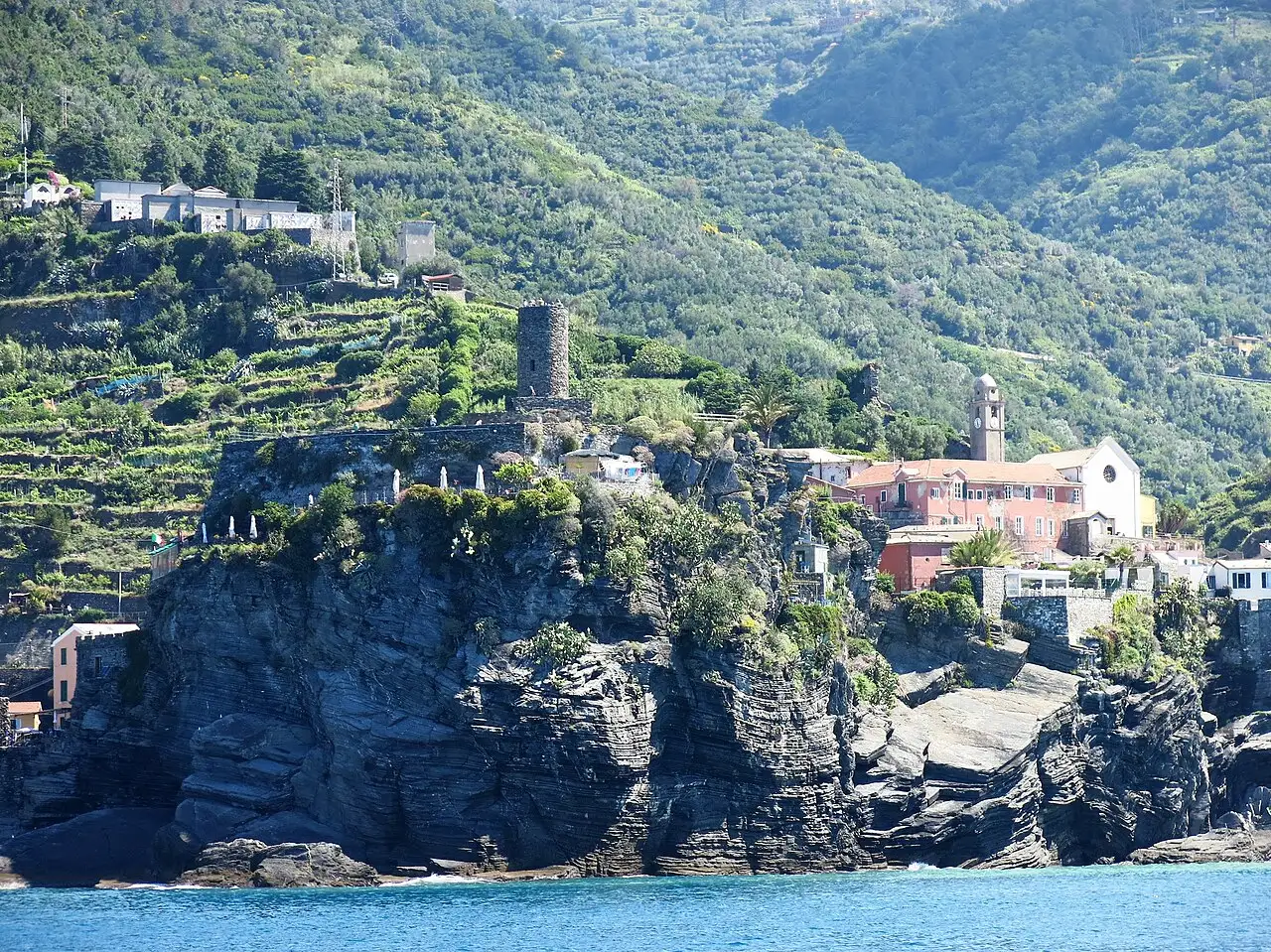 A torre redonda do Castello Doria no alto do rochedo escuro de Vernazza, sobre o mar, com casas e encostas em socalcos atrás.