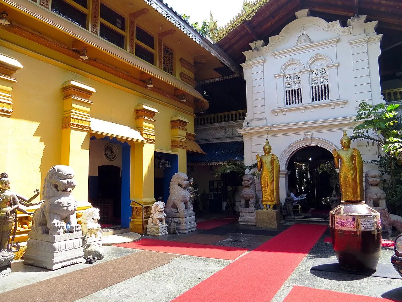 Estátua branca de leão guardião, com pequenas figuras douradas ao pé, num corredor de entrada.