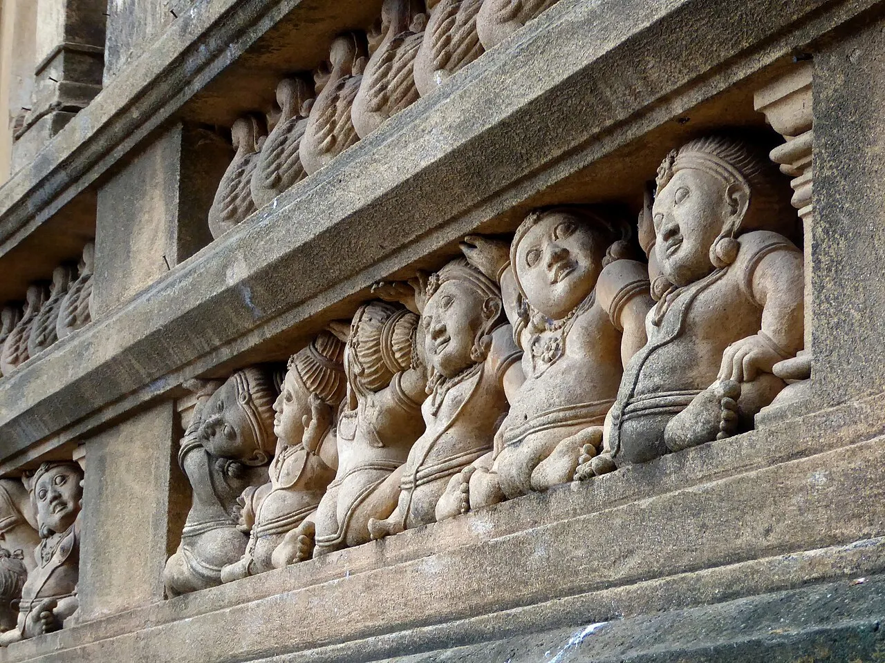 Rangée de petites figures sculptées dans une pierre claire, appuyées les unes contre les autres, sur une frise de temple.
