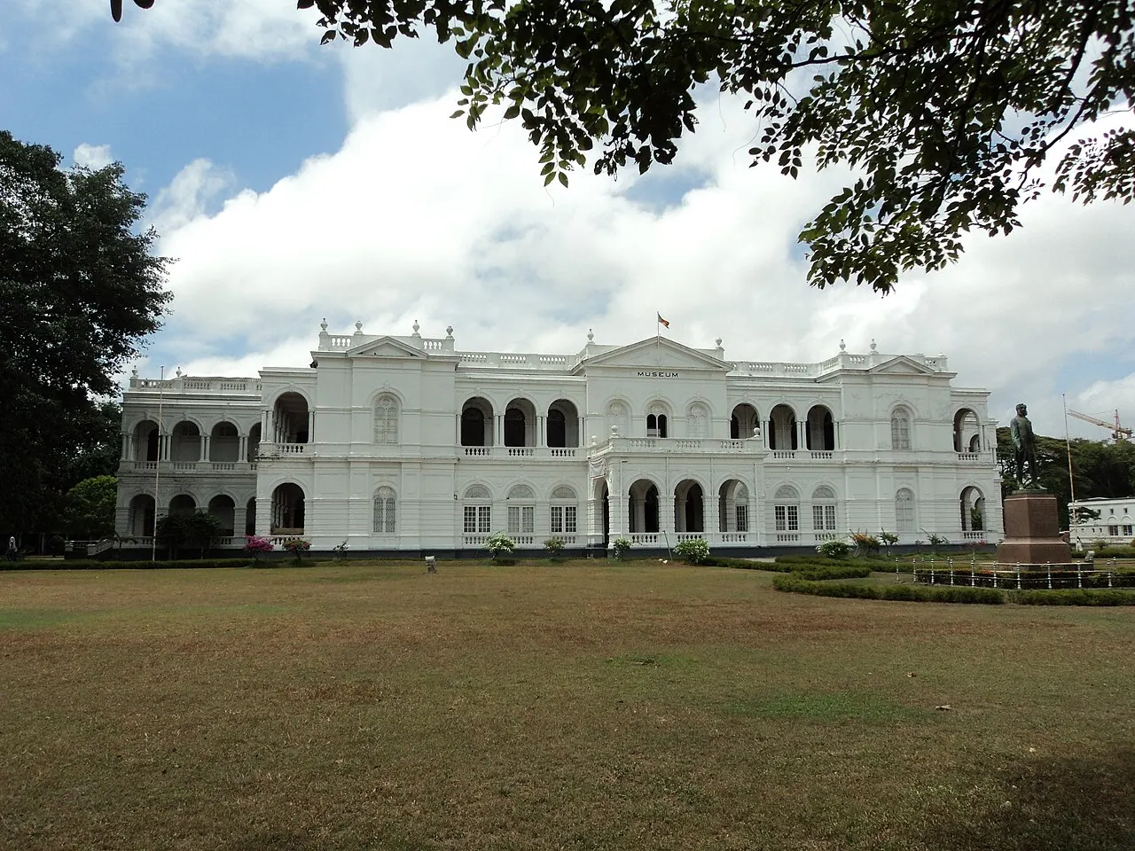 Prédio colonial branco de dois andares, com arcadas e varandas, atrás de um gramado.