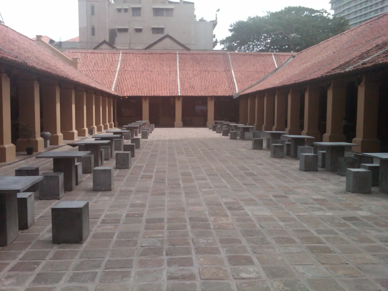 O pátio do Old Colombo Dutch Hospital tem telhados de telha, colunatas dos dois lados e mesas de concreto.