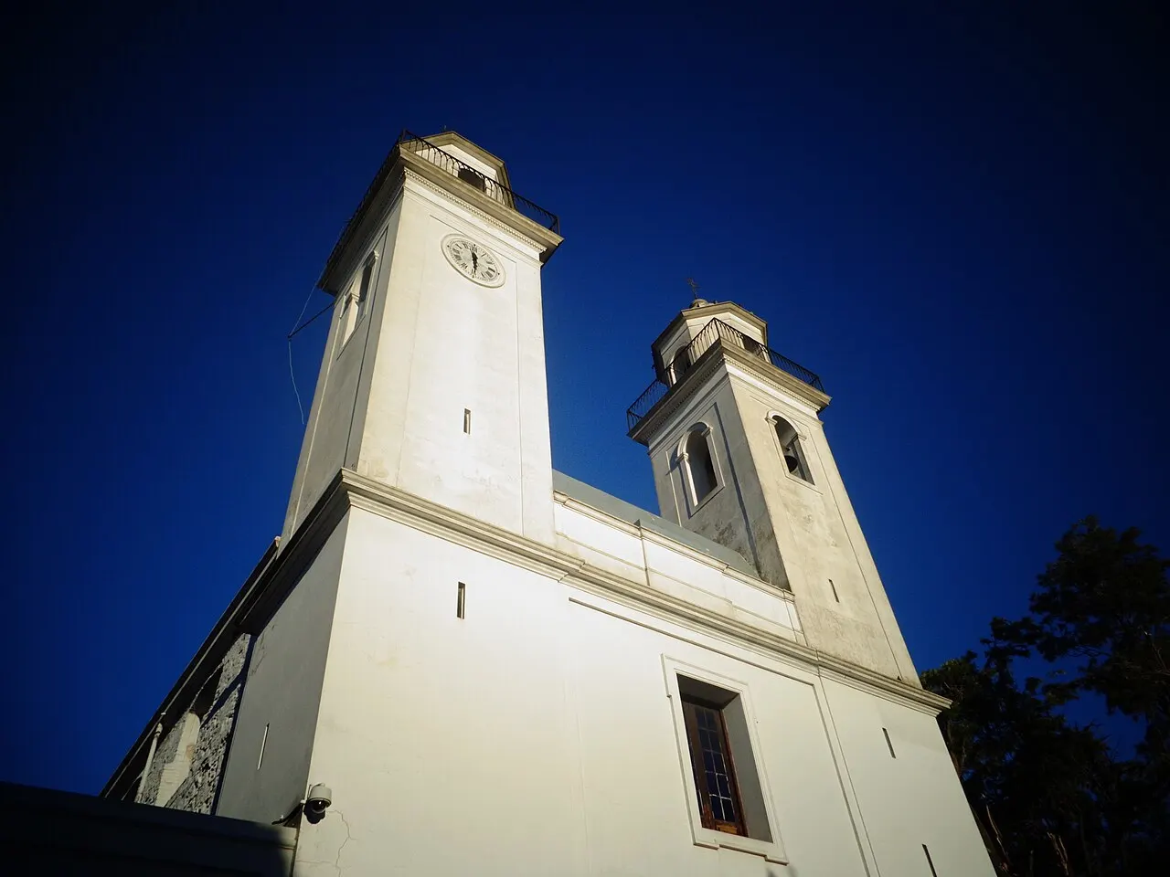 As duas torres brancas da Basílica do Santíssimo Sacramento, em Colonia del Sacramento, vistas de baixo contra um céu azul-escuro.