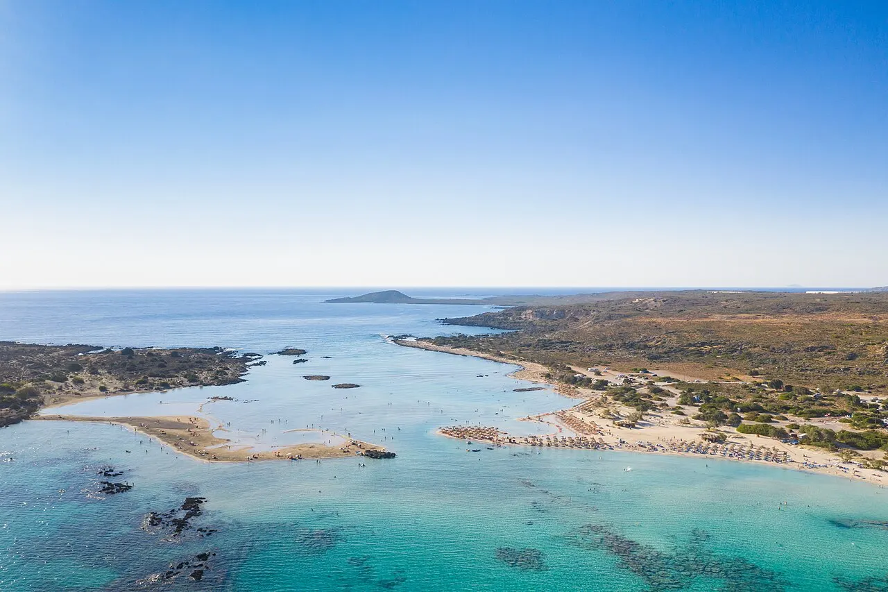 A praia de Elafonisi vista do alto, com a faixa de areia clara, a lagoa rasa turquesa e a ilha ao lado.