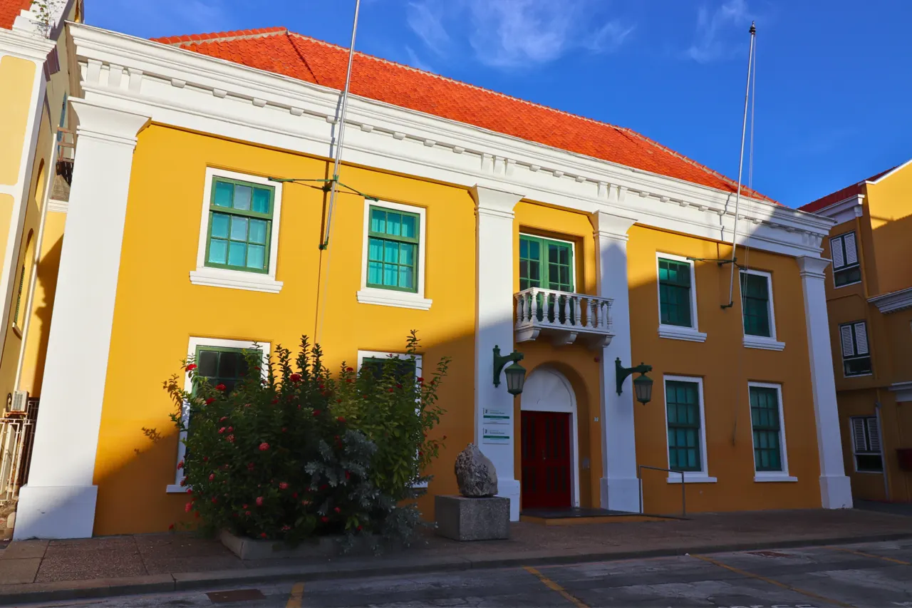 O prédio amarelo do palácio do governador dentro do Fort Amsterdam, com janelas verdes, telhado laranja e uma varanda branca.
