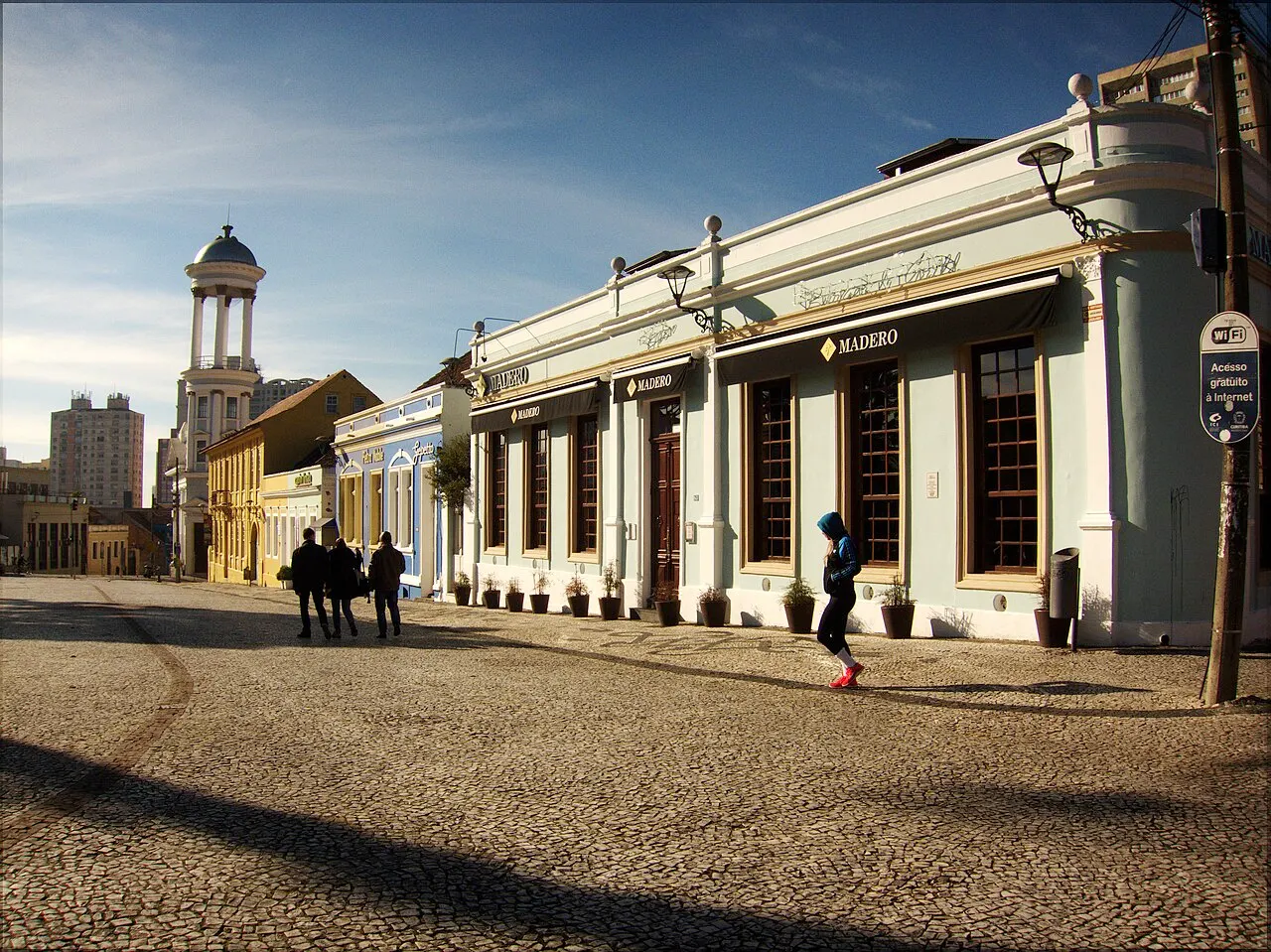 O calçamento de pedra do Largo da Ordem com o casario histórico ao redor e a torre de uma igreja ao fundo, sob sol forte.