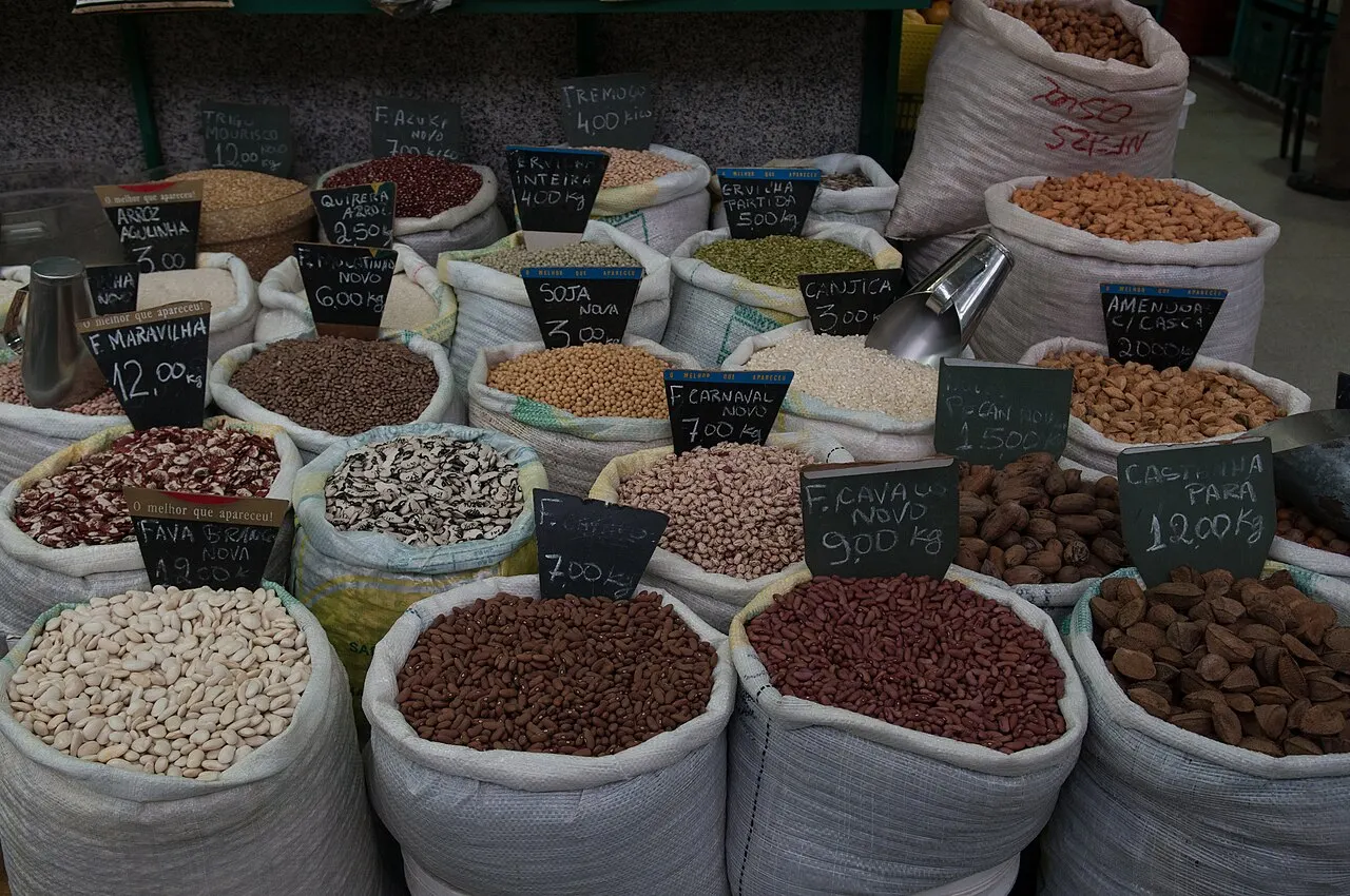 Sacos abertos de feijões, grãos e temperos com plaquinhas de preço numa banca do Mercado Municipal.