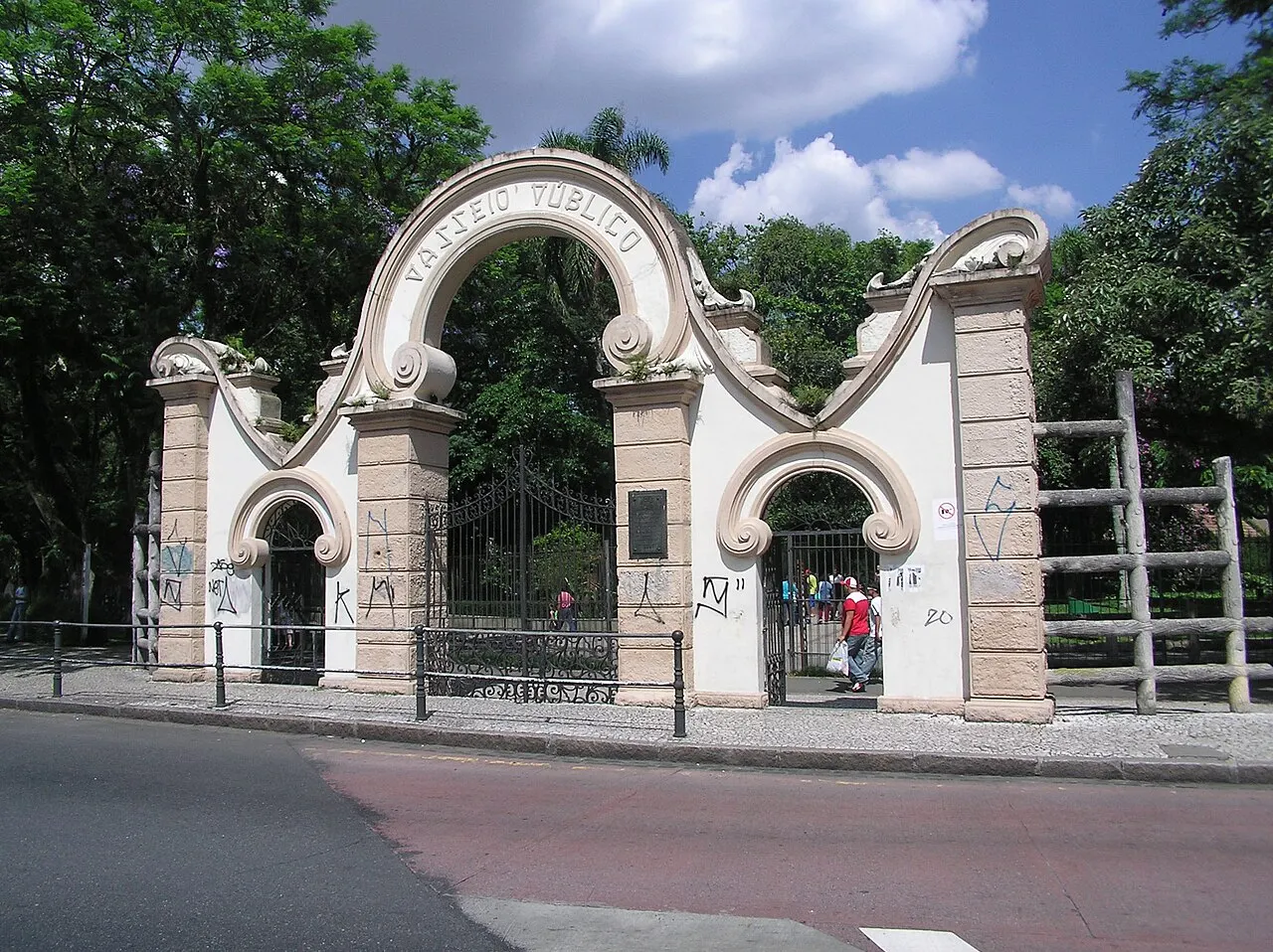 O portal de entrada do Passeio Público, branco e em arcos, com as árvores do parque atrás.