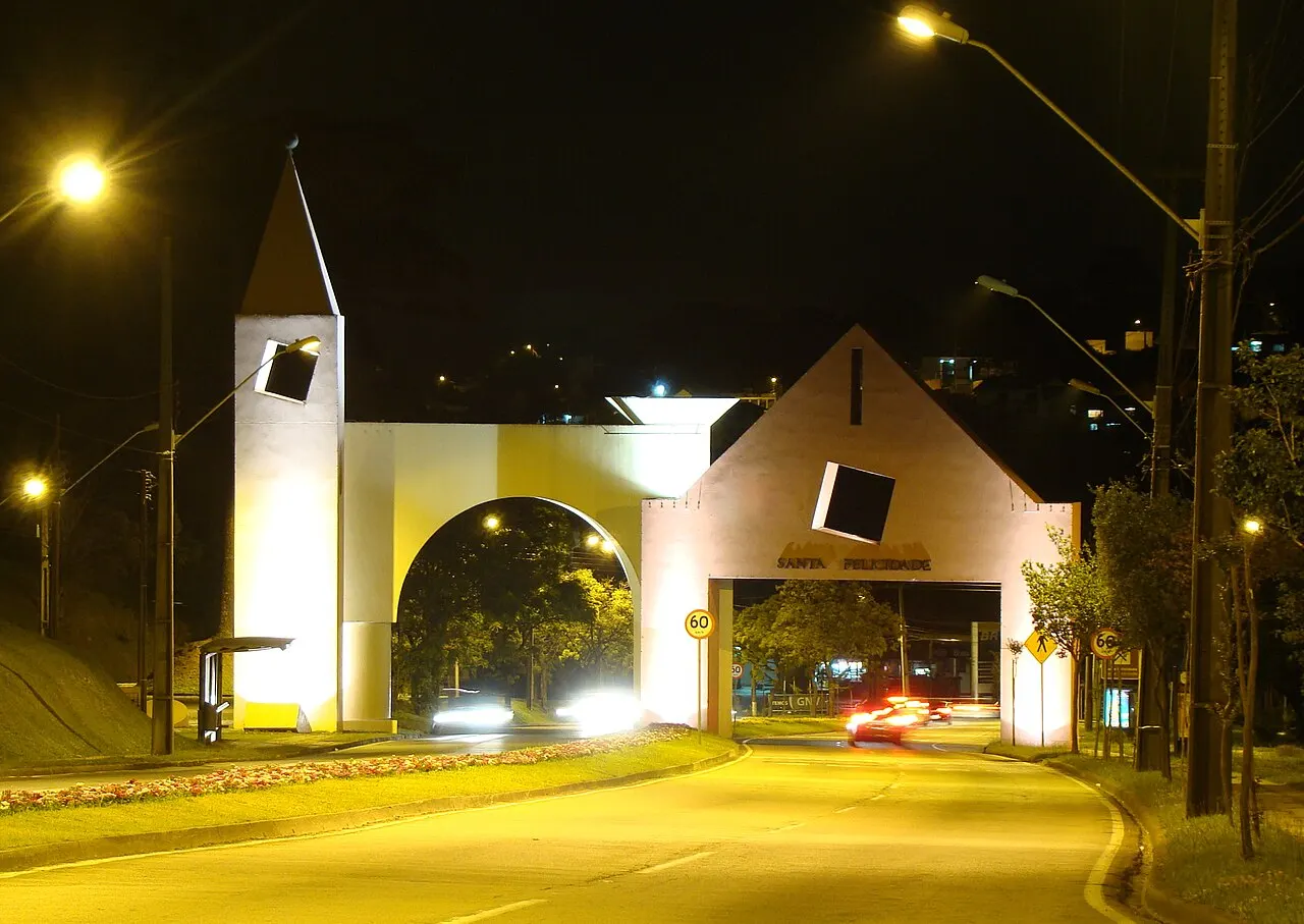 O portal de entrada do bairro de Santa Felicidade, com a torre e o arco iluminados à noite sobre a avenida.