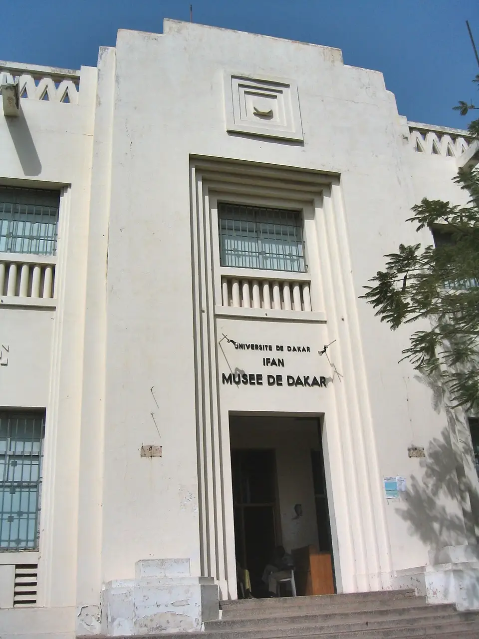 Fachada branca do museu, com frisos verticais e a placa IFAN e Musée de Dakar sobre a porta.