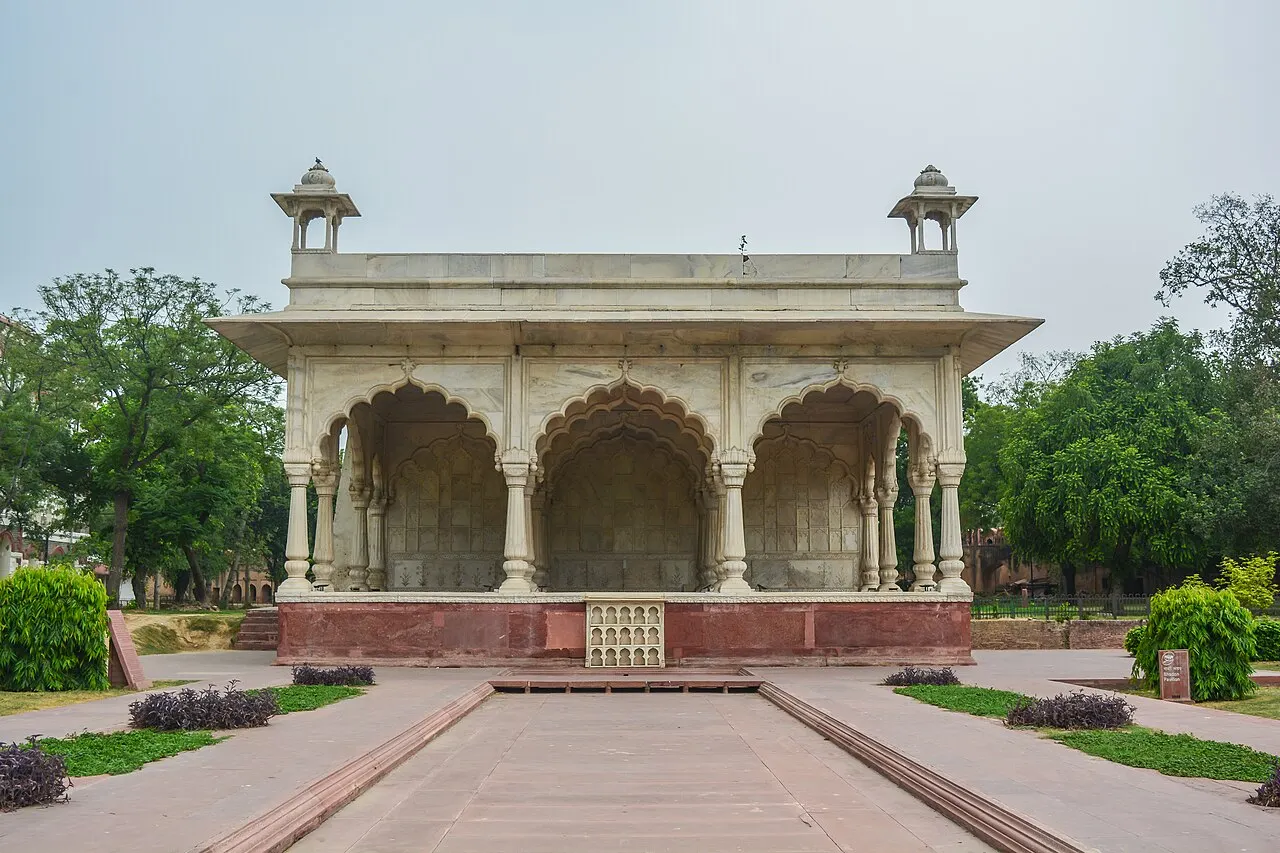 Pavilhão de mármore branco com arcos lobulados e pequenas cúpulas nos cantos, num jardim.