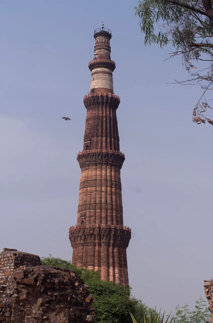 Minarete alto de arenito vermelho e claro, com varandas em anéis, sob céu azul.