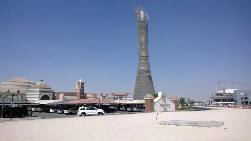 Torre alta de concreto e vidro que se alarga no topo, sobre prédios baixos, em dia claro.
