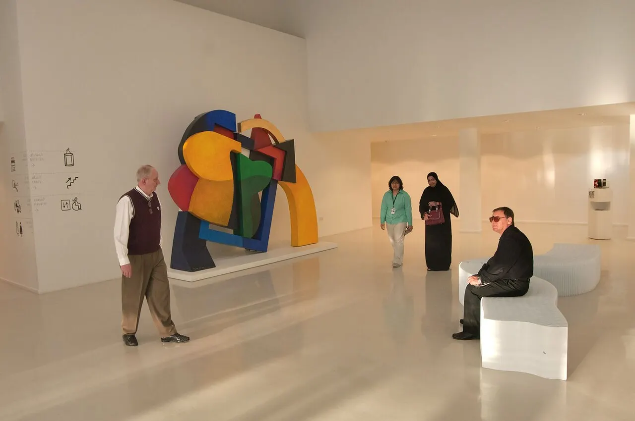 Sala do Mathaf com uma escultura geométrica colorida, piso claro e pessoas em pé e sentadas.
