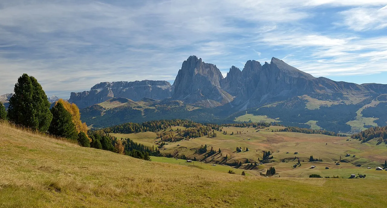Os prados ondulados da Alpe di Siusi no outono, com pinheiros e o Sassolungo e o Sassopiatto erguidos no horizonte.