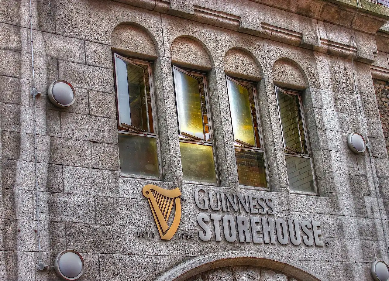 A parede de pedra cinza tem quatro janelas em arco, a harpa dourada e as letras Guinness Storehouse.