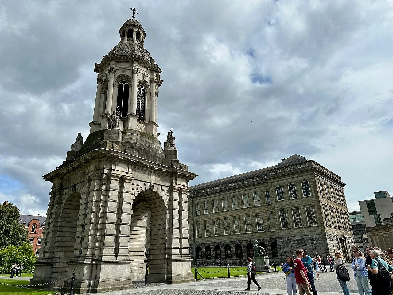 Campanário de pedra do Trinity College, em Dublin, no pátio, com estudantes e visitantes em volta.