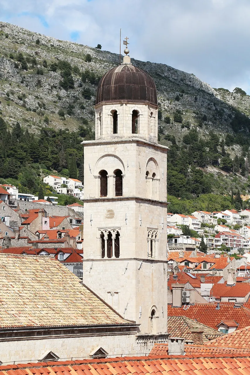 Campanário de pedra do mosteiro franciscano de Dubrovnik, com cúpula no alto, acima dos telhados.