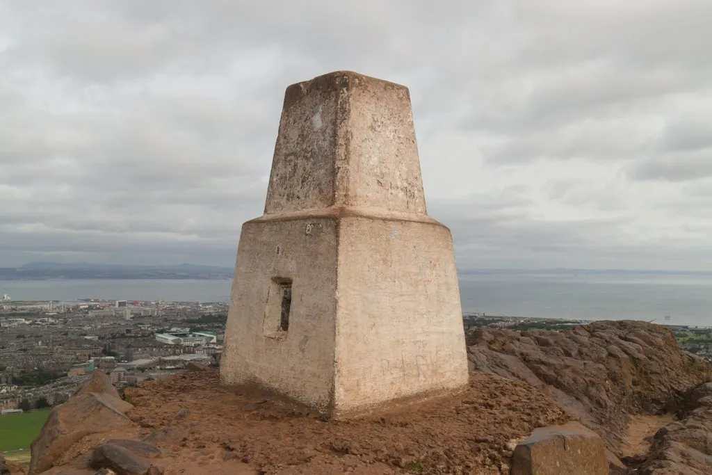 Pilar de concreto claro sobre rocha avermelhada no alto do morro, com a cidade e o mar ao fundo.