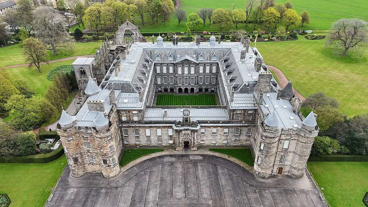 Vista aérea de um palácio de pedra com pátio quadrado, telhados de ardósia e jardins em volta.
