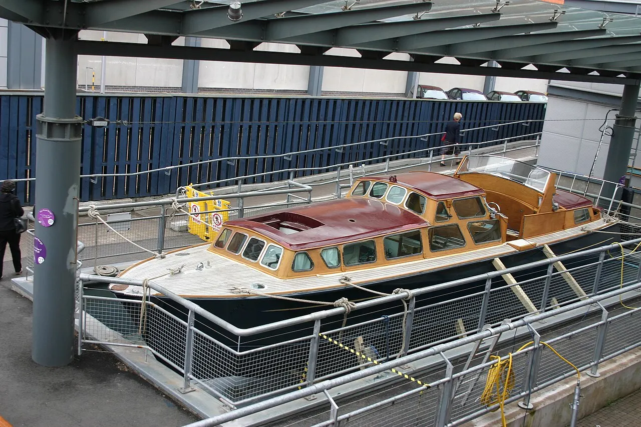 A lancha real do iate Britannia, de madeira envernizada com cabine, exposta num berço no cais de Leith, sob uma cobertura.