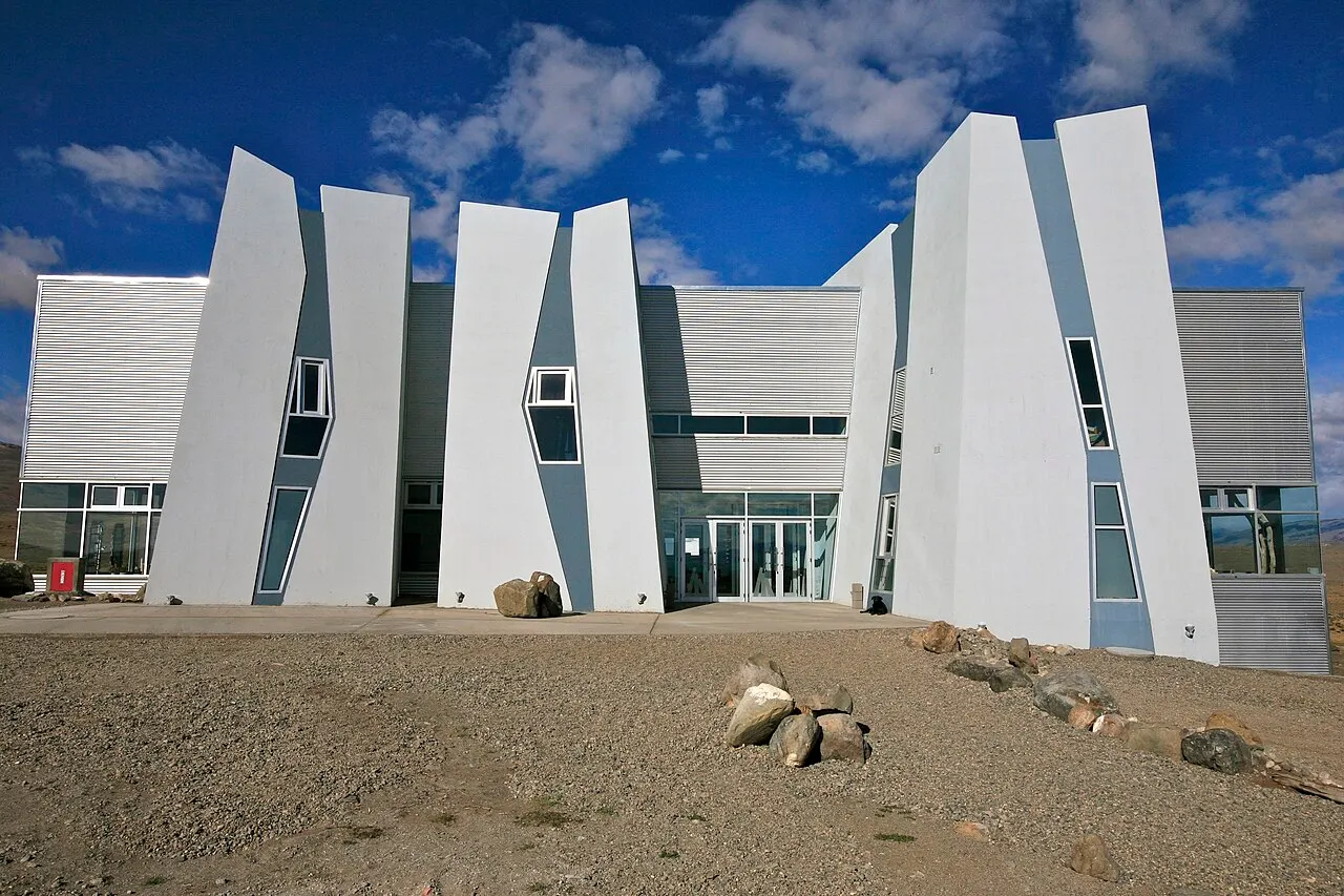 O prédio do Glaciarium, o museu do gelo patagônico, com placas brancas e angulosas na fachada, na estepe seca, sob céu azul.