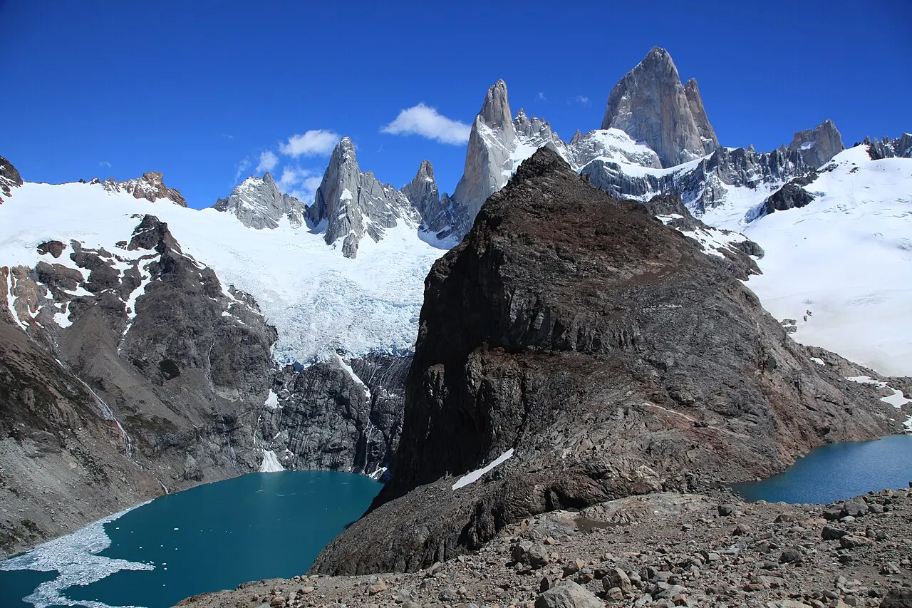 A Laguna de los Tres, de água azul-turquesa, ao pé das agulhas de granito do Fitz Roy cobertas de neve, sob céu azul.