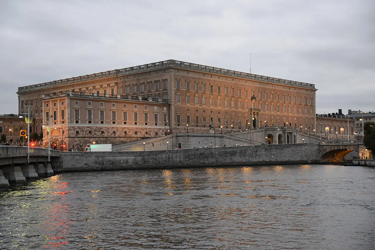Palácio Real de Estocolmo, bloco baixo e longo de pedra, visto da água ao entardecer.