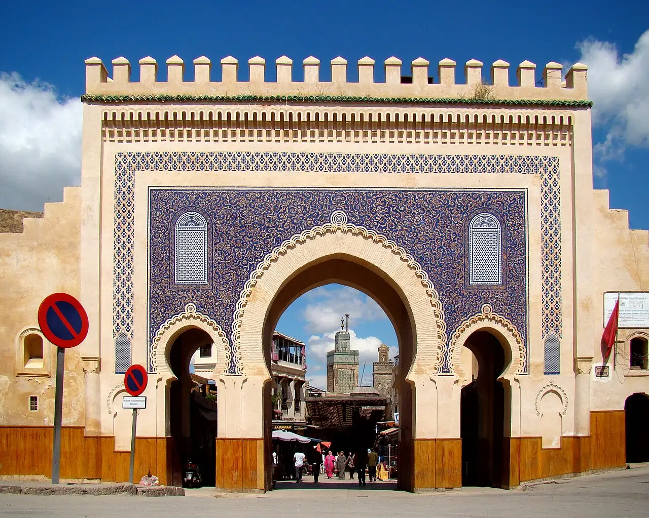 Porta de Bab Boujloud coberta de azulejo azul, com arco em ferradura, ameias e gente passando por baixo.