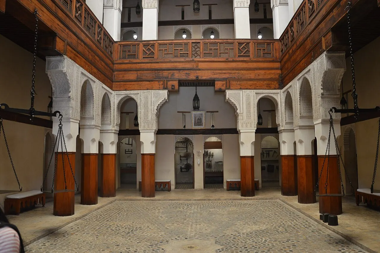 O pátio tem arcos brancos sobre pilares de madeira, uma galeria de madeira no alto e balanças grandes penduradas nas laterais.