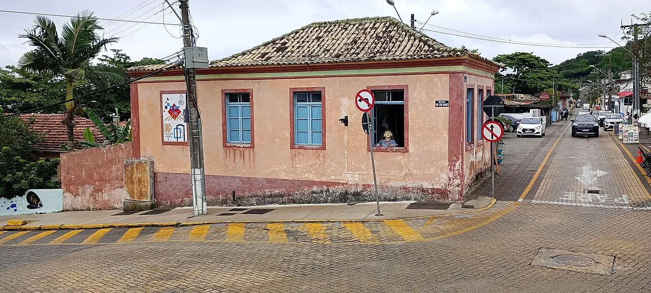 Uma casa térrea antiga, rosada, com janelas azuis e telhado de telha, na esquina de uma rua de paralelepípedo em Santo Antônio de Lisboa.