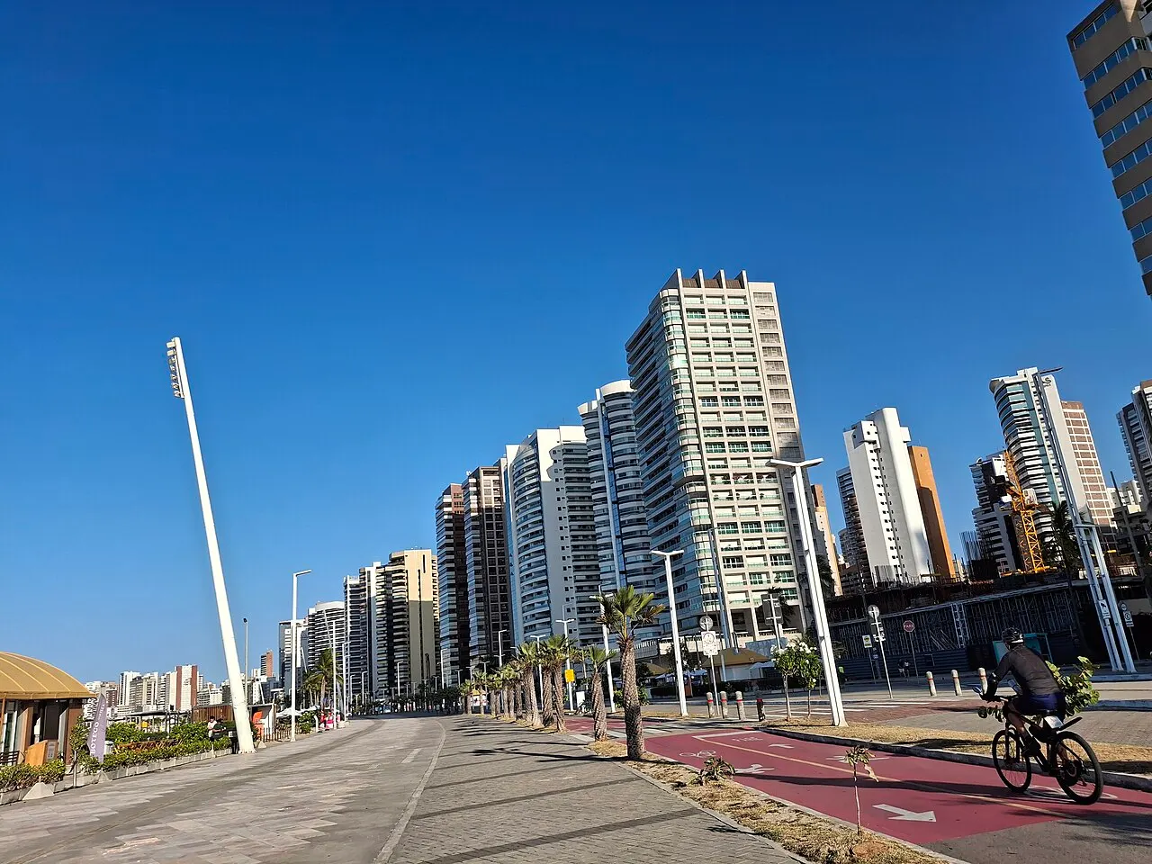 O calçadão da Avenida Beira-Mar com a ciclovia, um ciclista e a fileira de prédios altos de Meireles ao fundo.