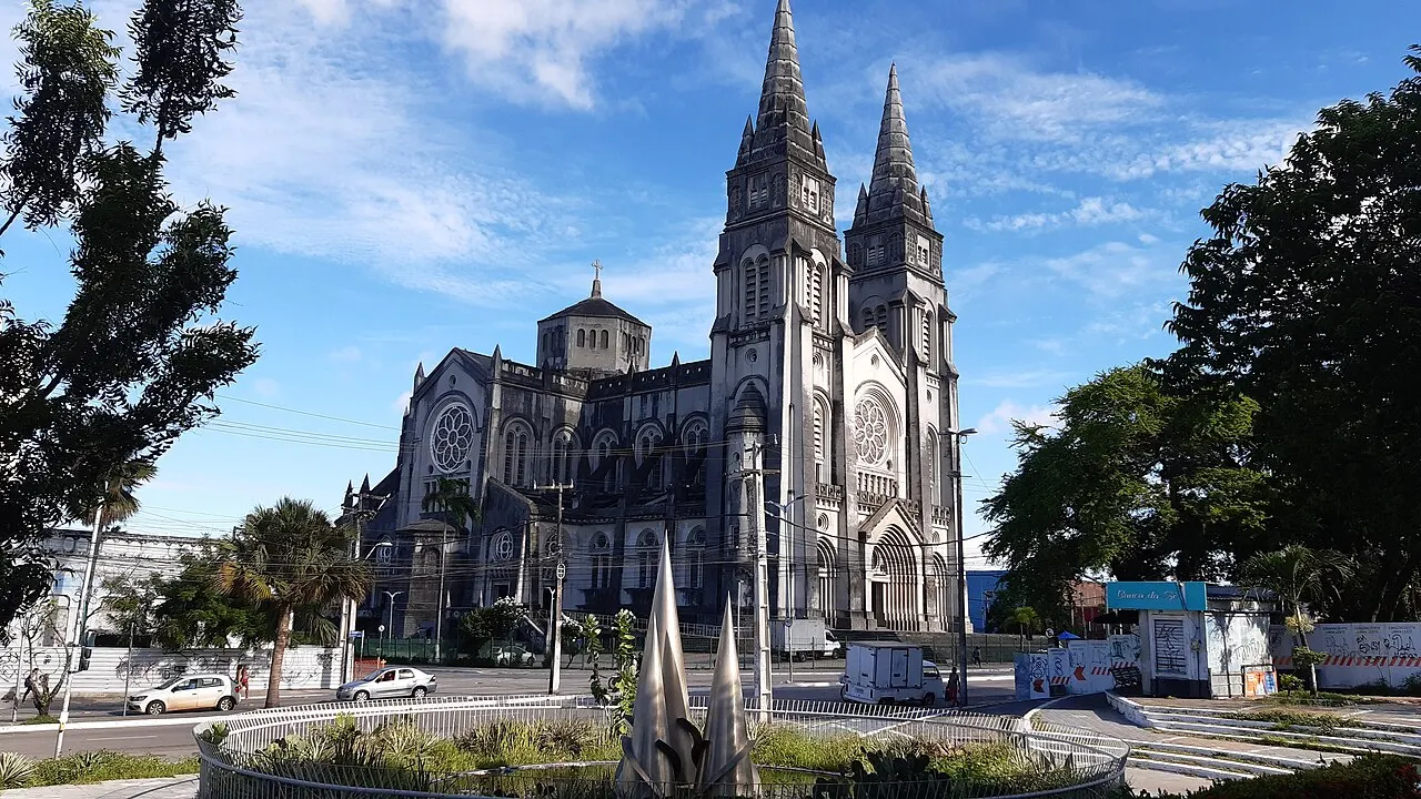 A Catedral Metropolitana de Fortaleza, de pedra cinza e duas torres pontudas, vista da praça em frente sob céu azul.