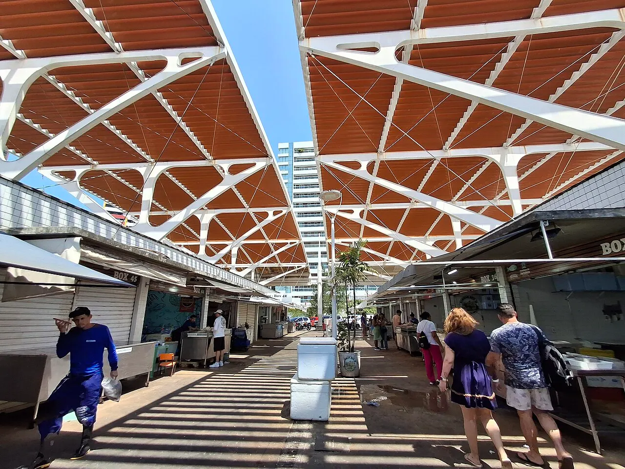O corredor do Mercado dos Peixes sob a cobertura de lonas em arcos, com as bancas dos dois lados e gente passando.