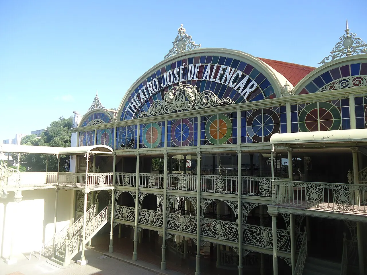 A estrutura de ferro verde e os vitrais coloridos do Theatro José de Alencar, com o nome em letras sobre o arco.