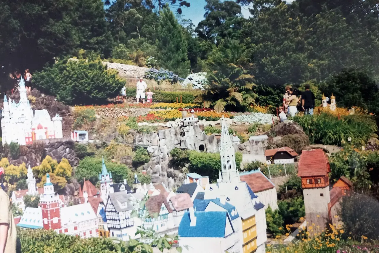 Miniaturas coloridas de castelos, igrejas e casas europeias no Mini Mundo, em Gramado, entre canteiros de flores e árvores.